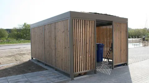 UNA containerskjul pulverlakeret og med lamelbeklædning og sedumtag