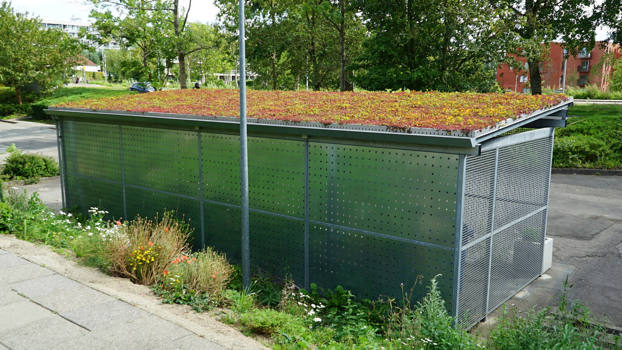 Stor PLAN containerskjulerrum med beklædning i hulplade og sedum på taget